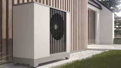 Moderne Wärmepumpe neben einem stilvollen Holzhaus Eine moderne Wärmepumpe steht neben einem Holzpaneel, umgeben von grünem Gras und einem gepflasterten Weg.